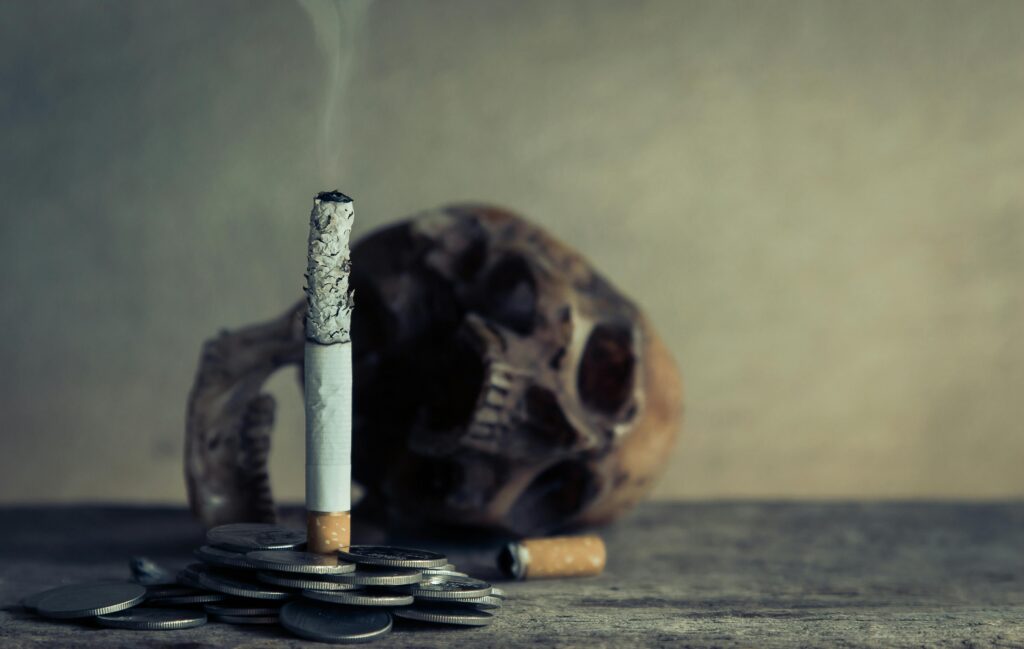 Burning cigarette in front of a broken skull.